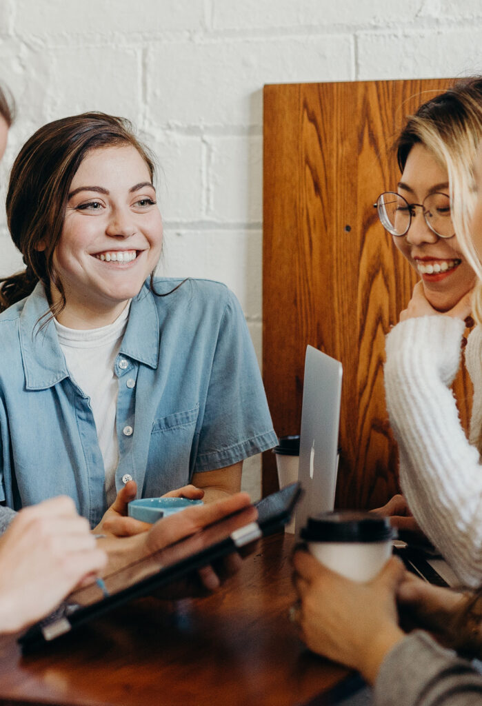 Two Smiling Women, One with Glasses, One in Denim Shirt Holding a Cup